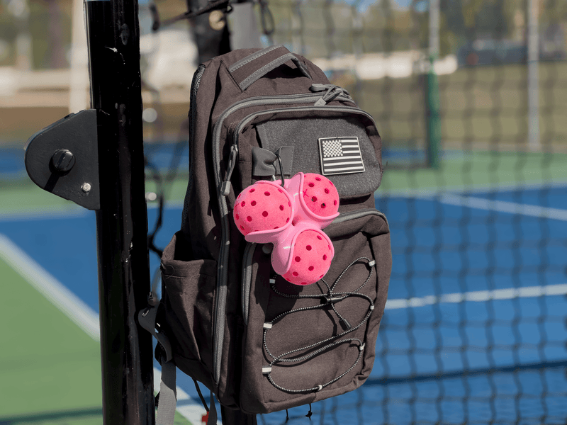 Pink Pickle Pocket attached to a black bag on a pickleball court.