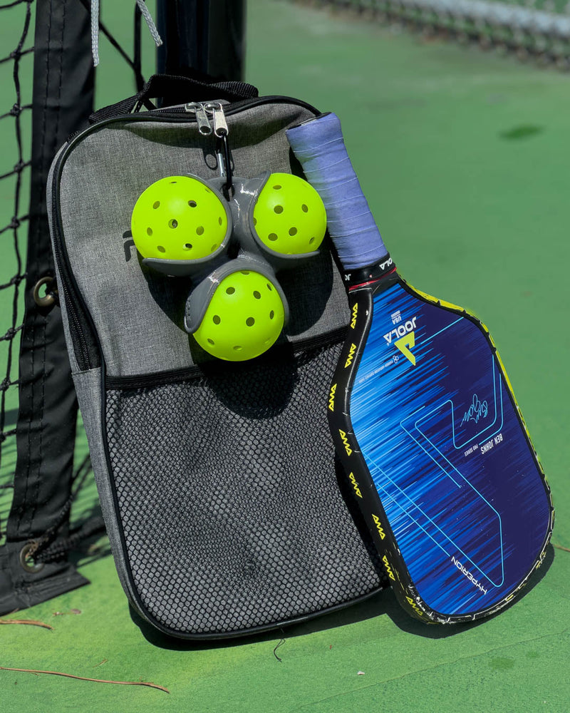 Blue pickleball paddle with green balls on a gray bag against a green court background